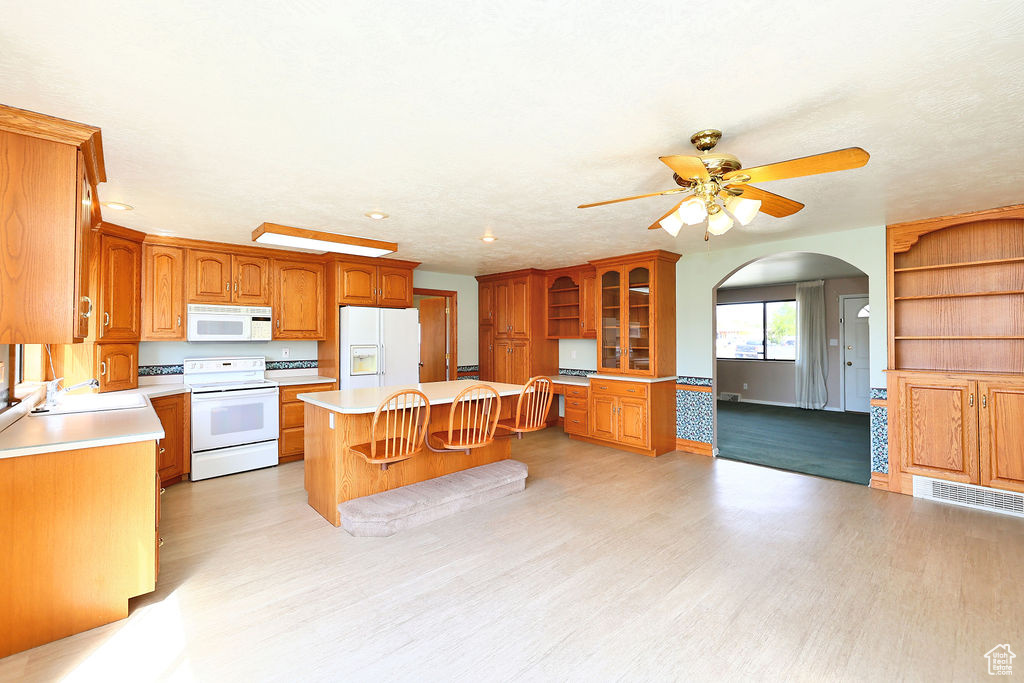 Kitchen featuring a breakfast bar, white appliances, light wood-type flooring, sink, and ceiling fan
