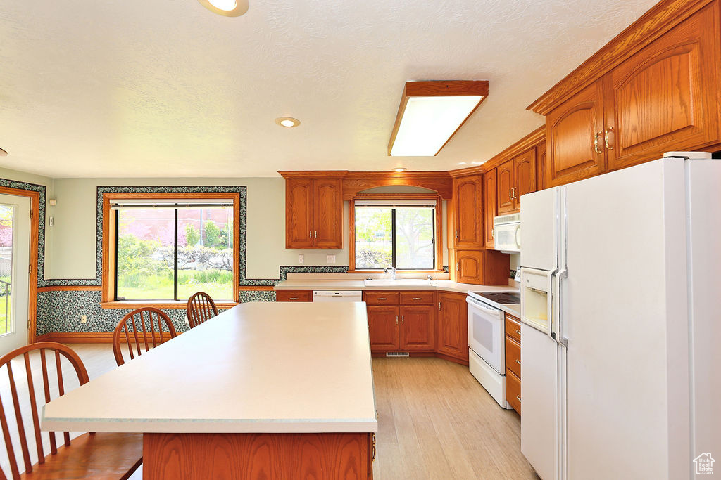 Kitchen featuring white appliances, light hardwood / wood-style flooring, sink, a breakfast bar area, and a kitchen island