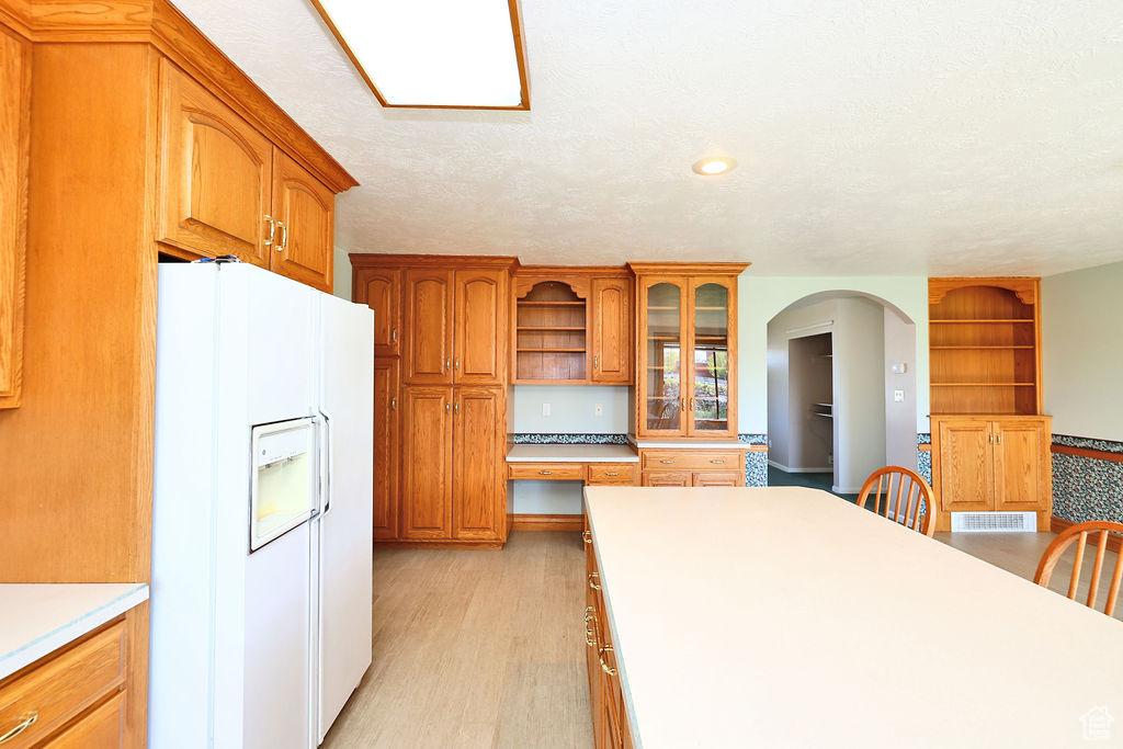 Kitchen featuring white fridge with ice dispenser, light hardwood / wood-style flooring, built in desk, and a textured ceiling