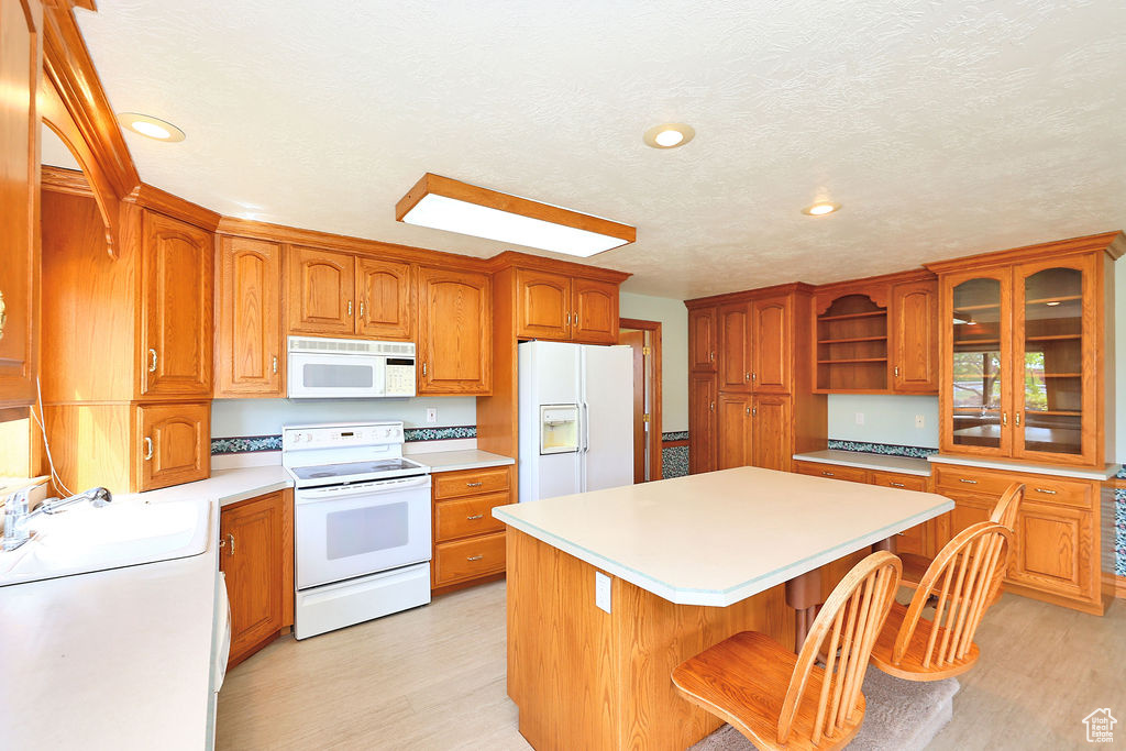 Kitchen featuring a kitchen island, sink, white appliances, light hardwood / wood-style flooring, and a kitchen breakfast bar