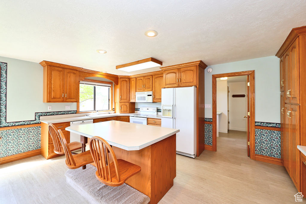 Kitchen with light hardwood / wood-style floors, white appliances, a kitchen island, and a breakfast bar