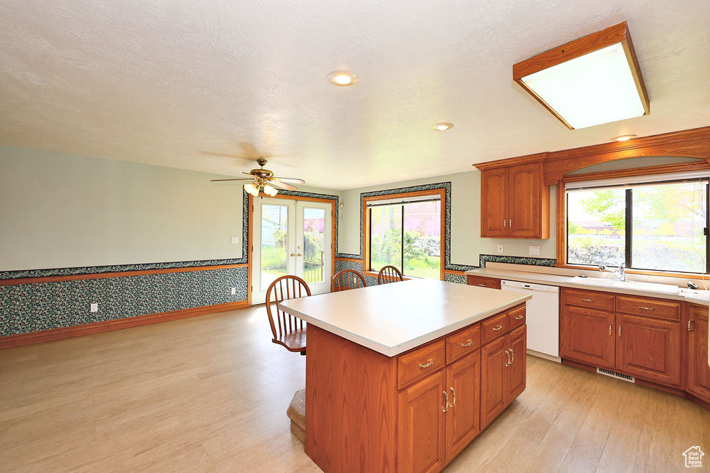 Kitchen with a wealth of natural light, light hardwood / wood-style floors, dishwasher, and a center island