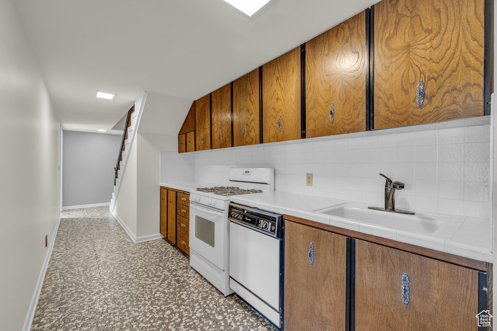 Kitchen featuring white appliances, tile counters, backsplash, sink, and light tile floors