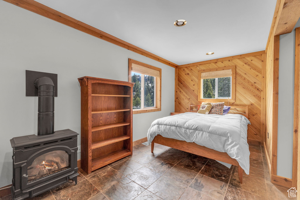 Tiled bedroom with ornamental molding, a wood stove, wood walls, and multiple windows