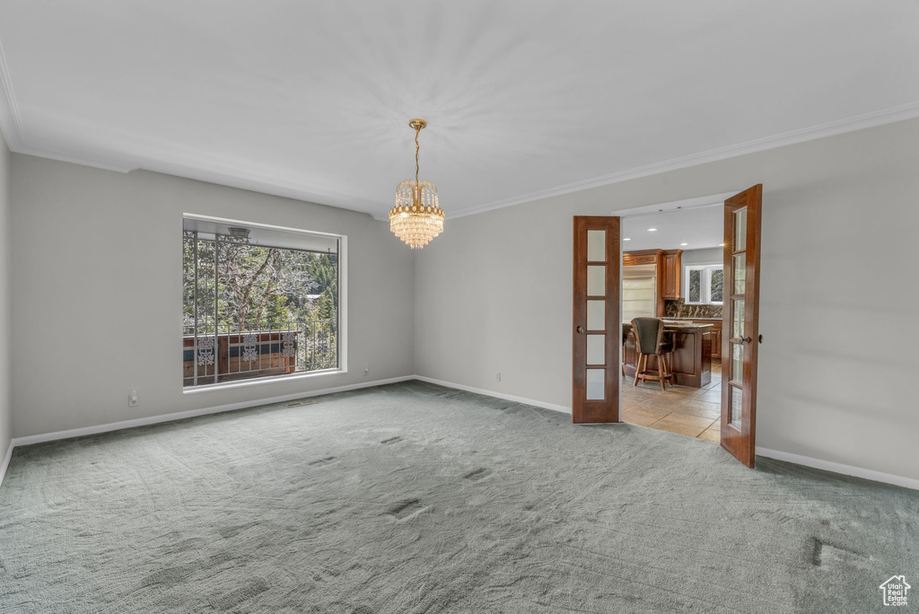 Unfurnished room featuring carpet floors, an inviting chandelier, crown molding, and french doors