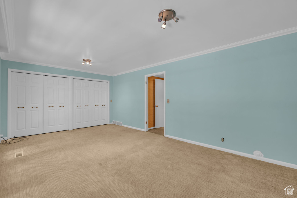 Unfurnished bedroom with ornamental molding, two closets, and carpet floors