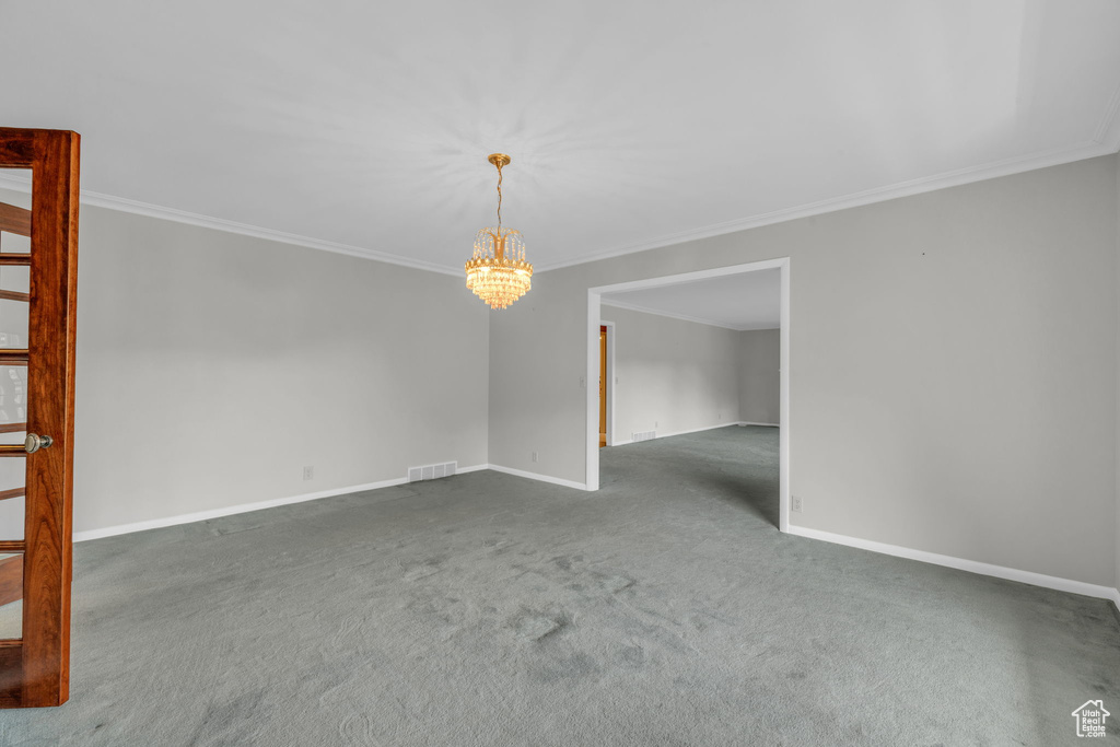 Carpeted empty room featuring crown molding and a chandelier