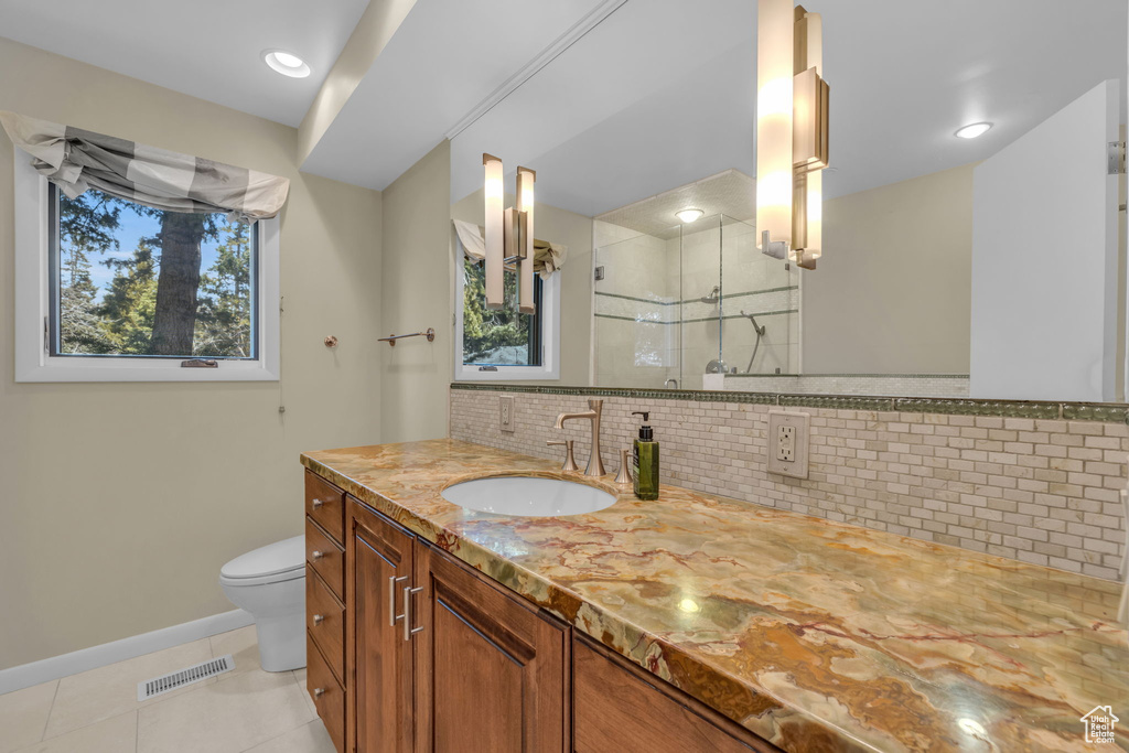 Bathroom featuring backsplash, large vanity, toilet, tile flooring, and tiled shower