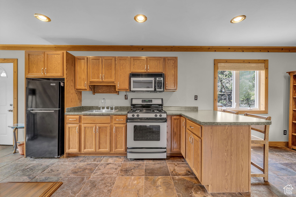 Kitchen featuring black refrigerator, stainless steel gas range oven, kitchen peninsula, tile flooring, and sink