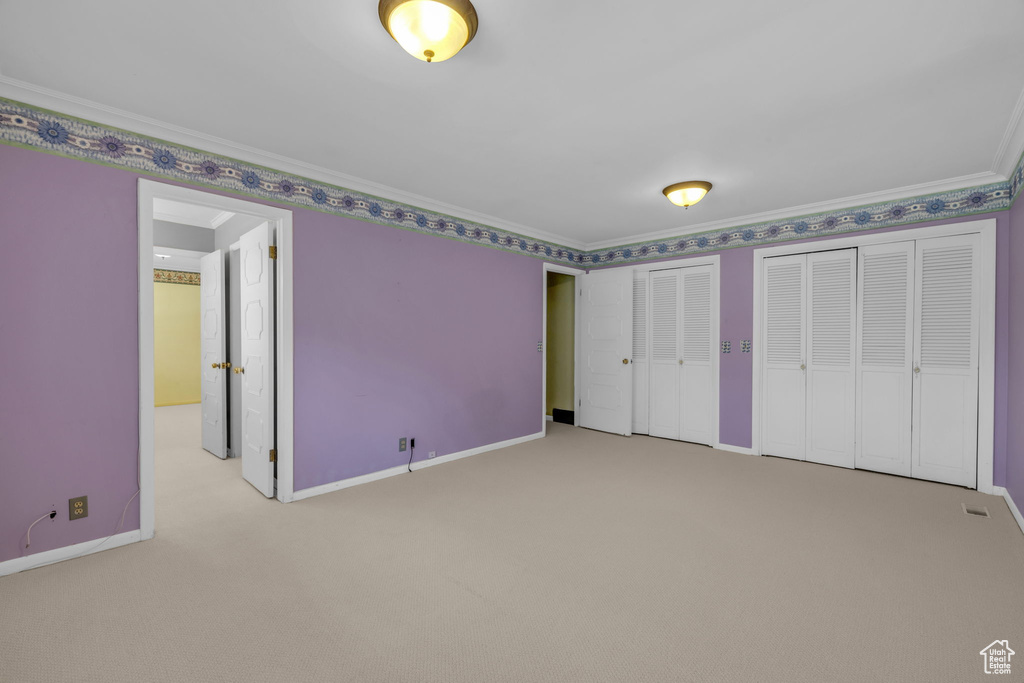 Unfurnished bedroom with carpet, two closets, and crown molding