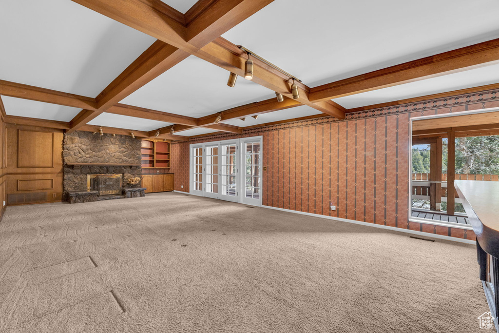 Unfurnished living room featuring beam ceiling, carpet, coffered ceiling, and a stone fireplace