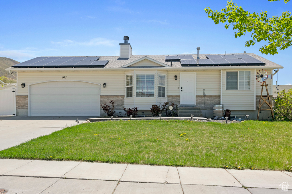 Ranch-style home with solar panels, a garage, and a front lawn