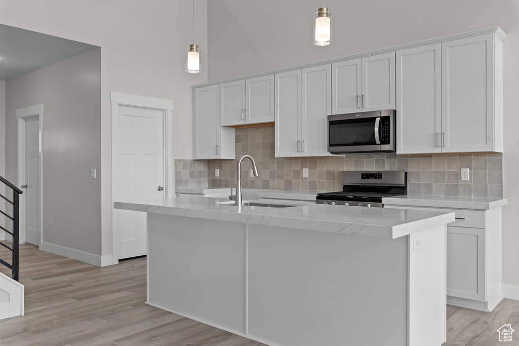 Kitchen with white cabinets, appliances with stainless steel finishes, pendant lighting, and a kitchen island with sink