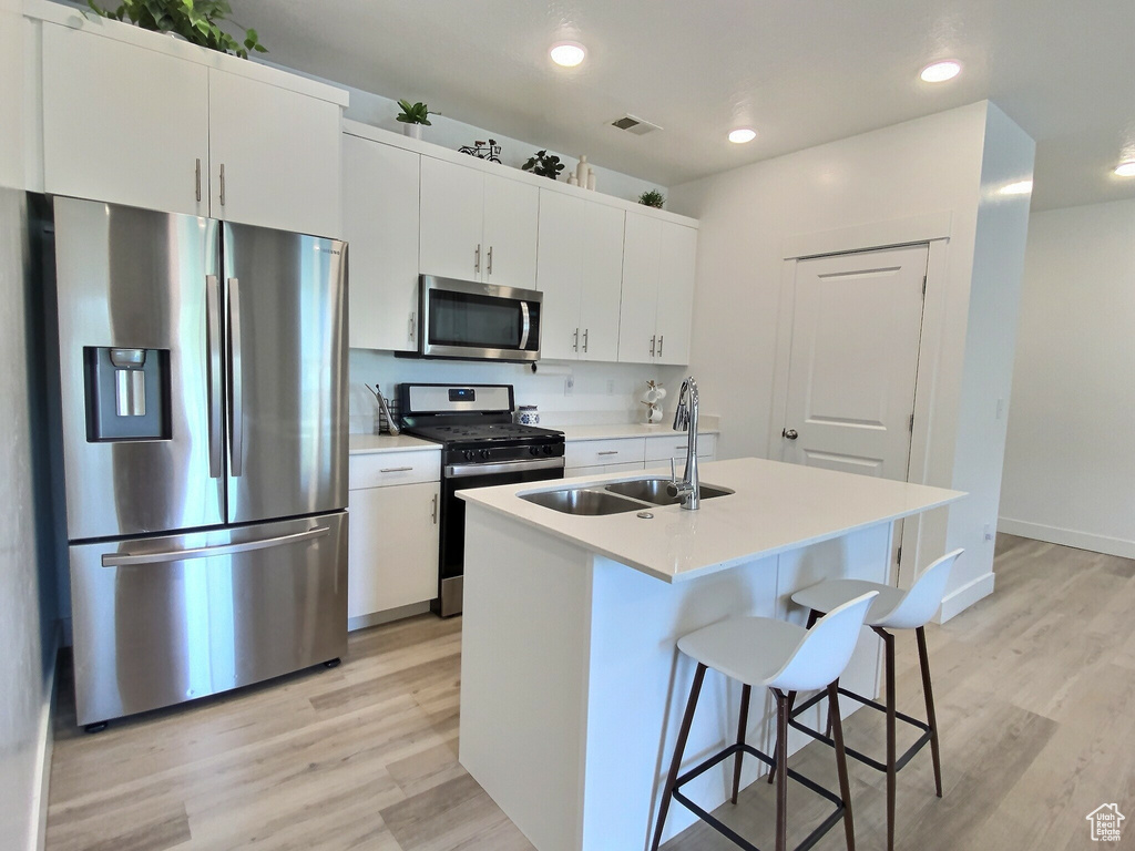Kitchen featuring white cabinets, stainless steel appliances, light wood-type flooring, and a kitchen island with sink