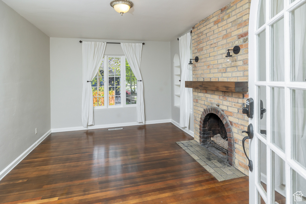 Unfurnished living room with dark wood-type flooring and a brick fireplace