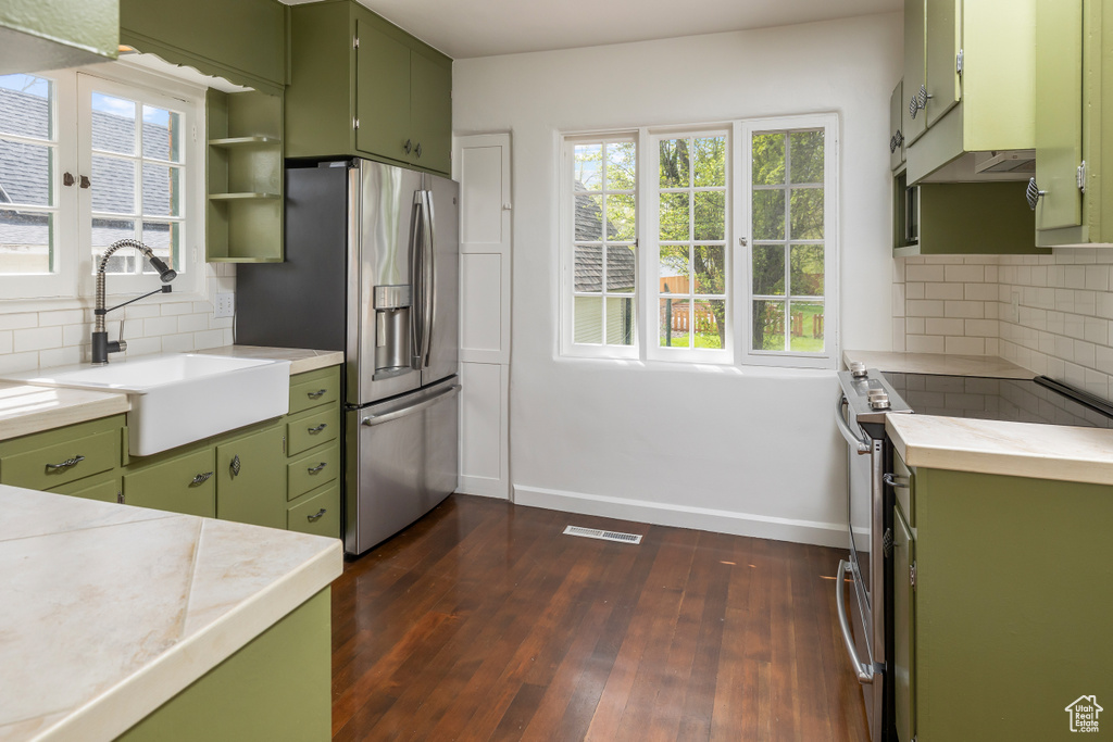 Kitchen featuring sink, backsplash, dark hardwood / wood-style flooring, stainless steel appliances, and green cabinetry
