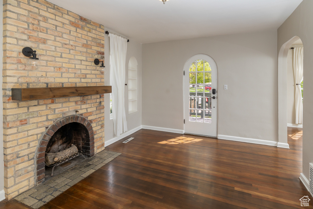 Unfurnished living room with dark wood-type flooring, brick wall, and a brick fireplace