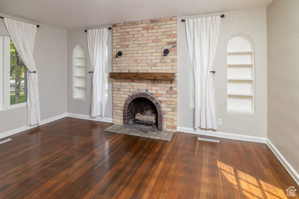 Unfurnished living room featuring wood-type flooring, built in features, and a brick fireplace