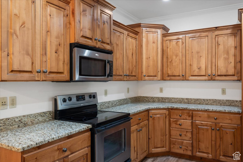 Kitchen with hardwood / wood-style flooring, crown molding, appliances with stainless steel finishes, and light stone counters