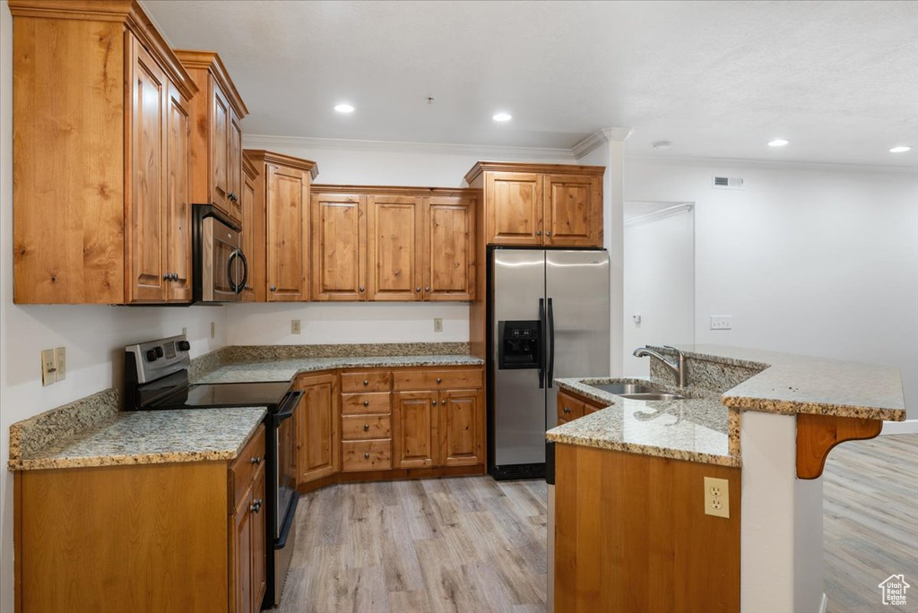 Kitchen featuring sink, a breakfast bar area, crown molding, stainless steel appliances, and light hardwood / wood-style flooring