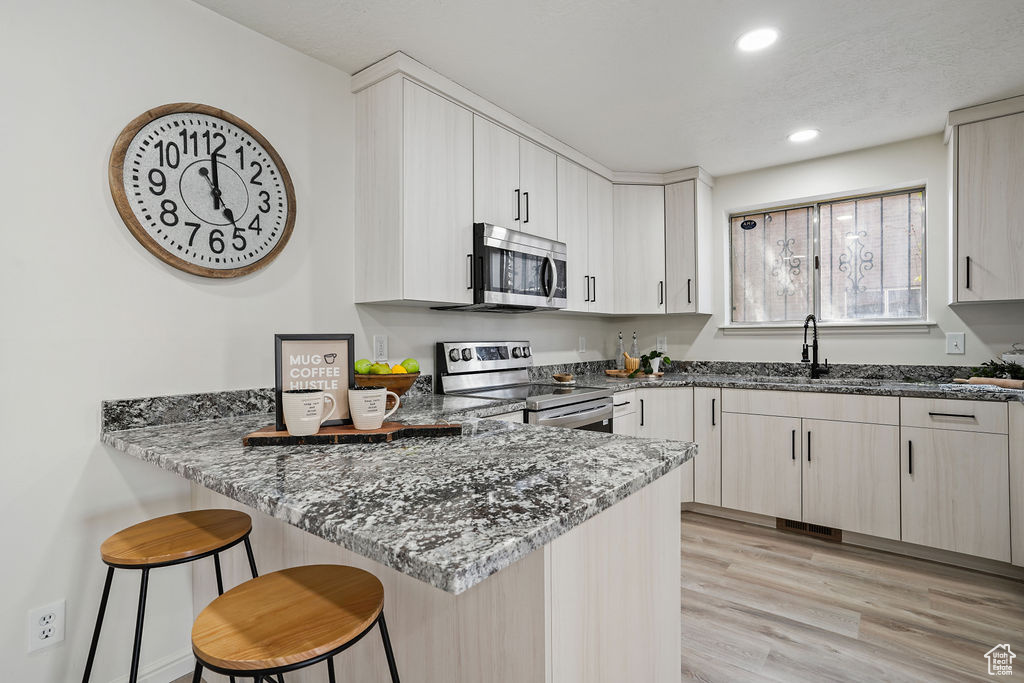Kitchen with stone counters, stainless steel appliances, light hardwood / wood-style floors, and a breakfast bar