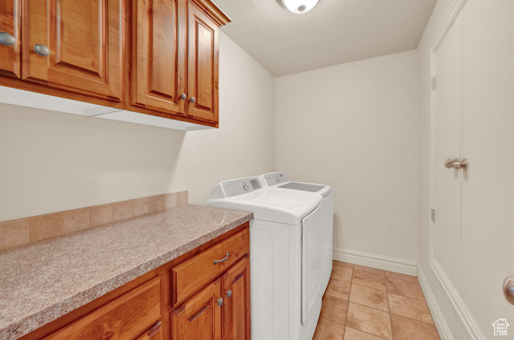 Clothes washing area featuring cabinets, washer and dryer, and light tile floors