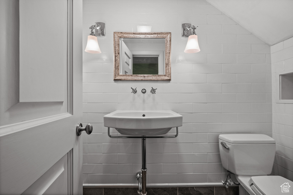 Bathroom featuring sink, tile walls, lofted ceiling, and toilet