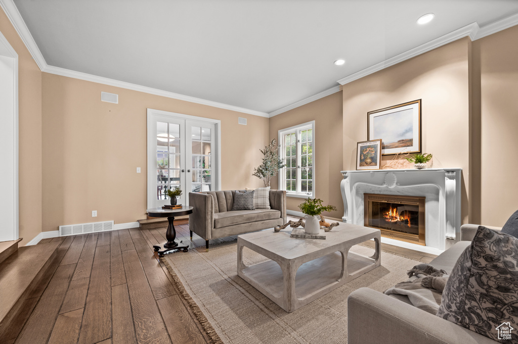 Living room with french doors, a high end fireplace, wood-type flooring, and crown molding
