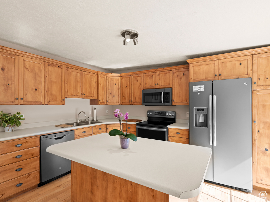 Kitchen with sink, appliances with stainless steel finishes, light hardwood / wood-style flooring, and a kitchen island