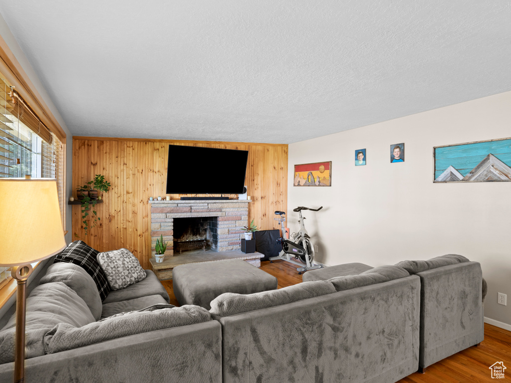 Living room with wood-type flooring, a fireplace, wood walls, and a textured ceiling