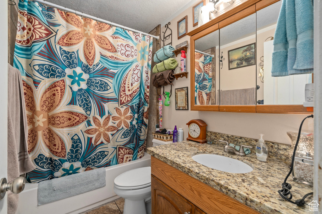 Full bathroom with vanity with extensive cabinet space, toilet, tile flooring, a textured ceiling, and shower / tub combo with curtain
