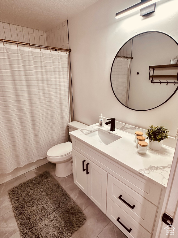 Bathroom featuring tile flooring, vanity, toilet, and a textured ceiling