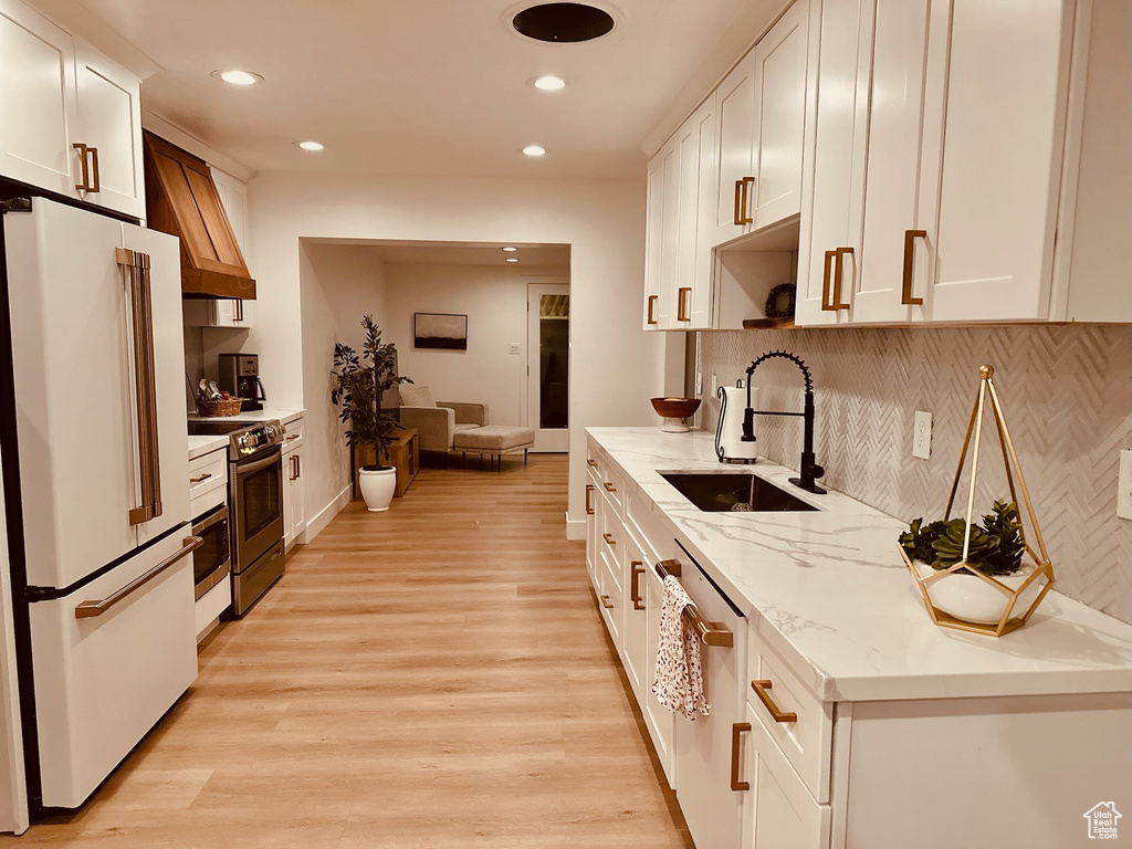 Kitchen featuring high end fridge, white cabinetry, backsplash, sink, and light hardwood / wood-style floors