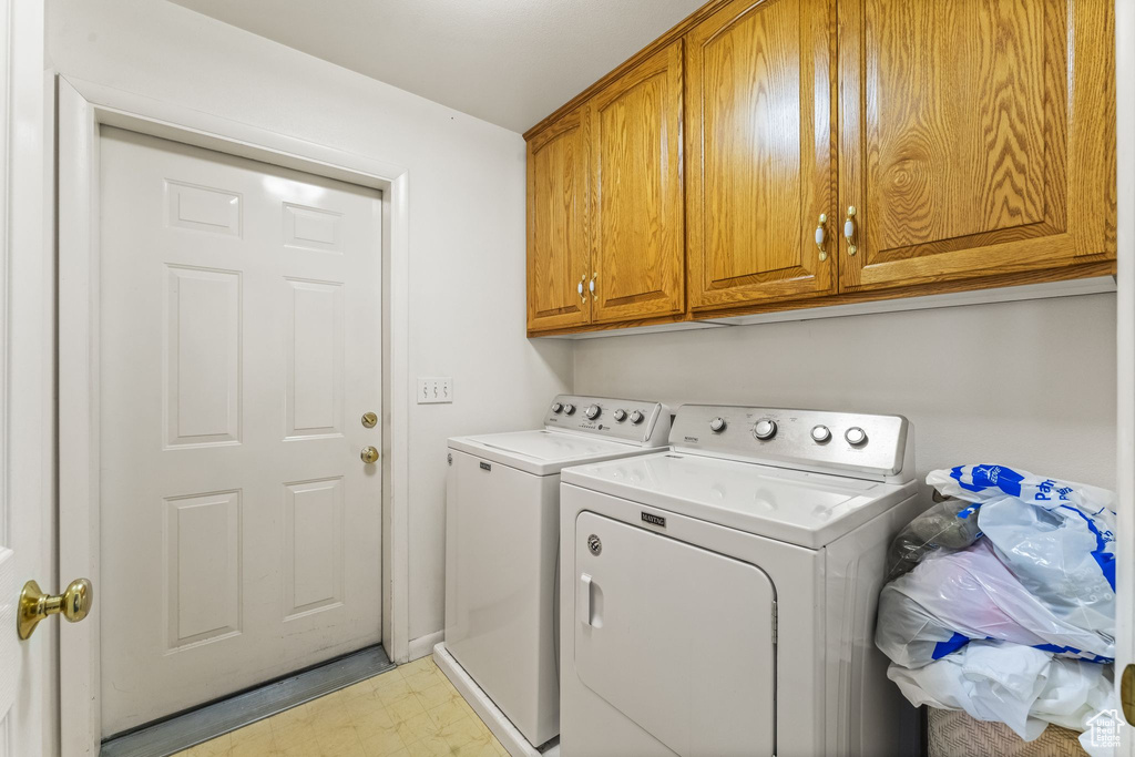 Laundry room with washing machine and clothes dryer, cabinets, and light tile floors
