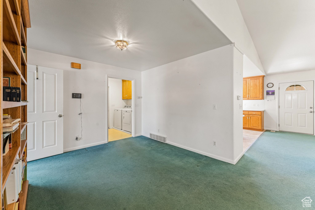 Carpeted spare room featuring lofted ceiling and independent washer and dryer