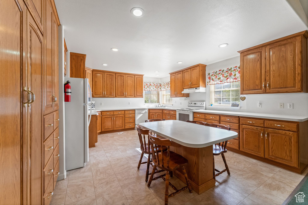 Kitchen with a kitchen island, a breakfast bar area, white appliances, light tile flooring, and sink