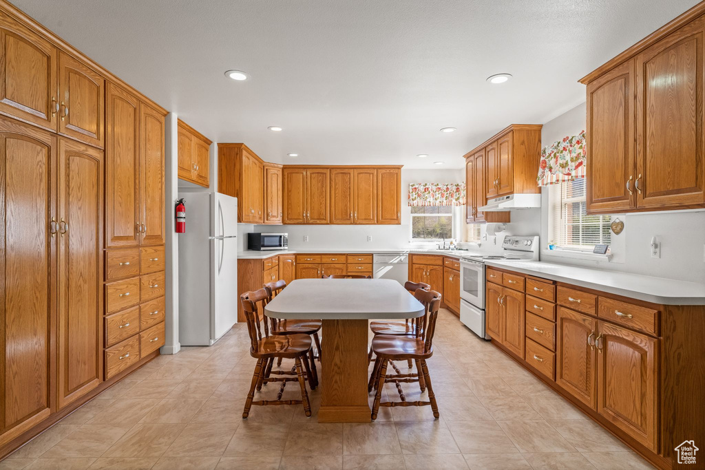 Kitchen featuring light tile floors, white appliances, a center island, and a breakfast bar