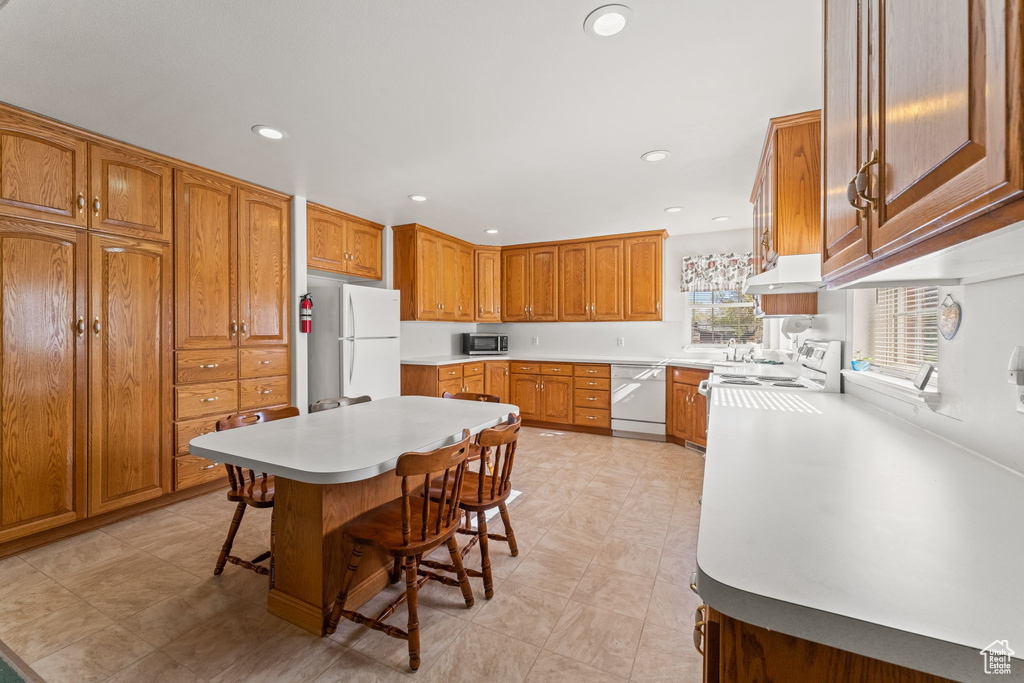 Kitchen featuring a center island, a breakfast bar, light tile floors, and white appliances