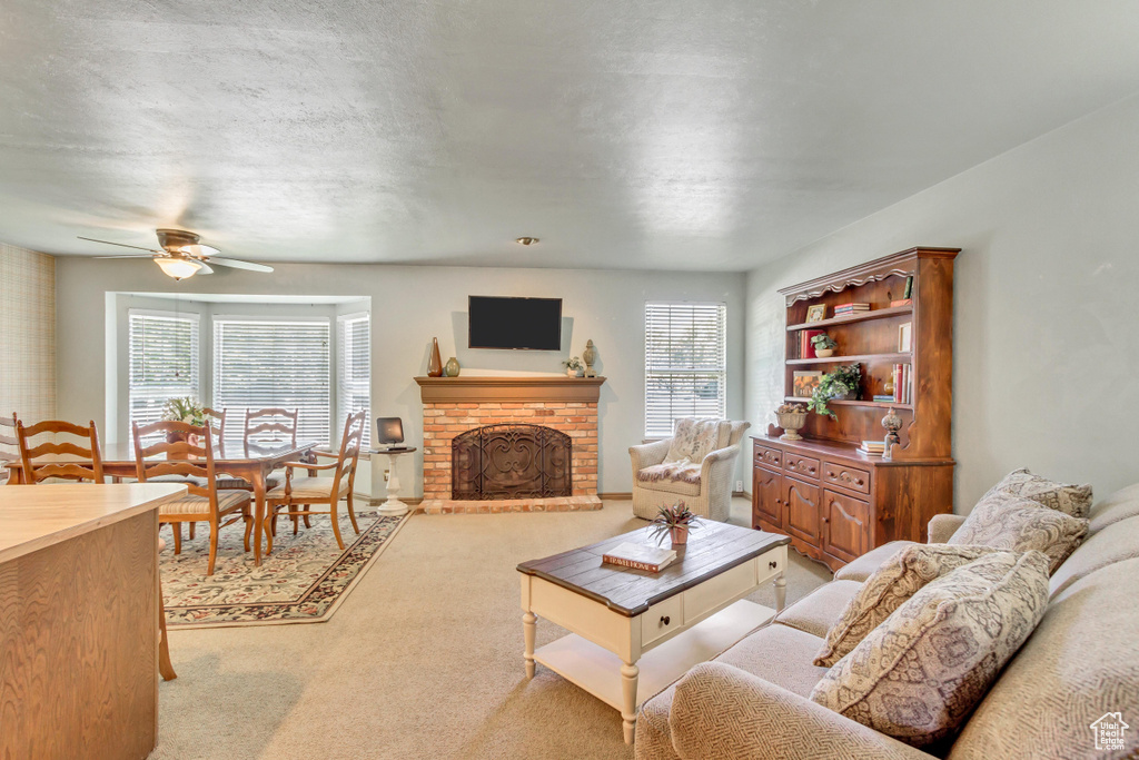 Carpeted living room featuring plenty of natural light, a fireplace, and ceiling fan