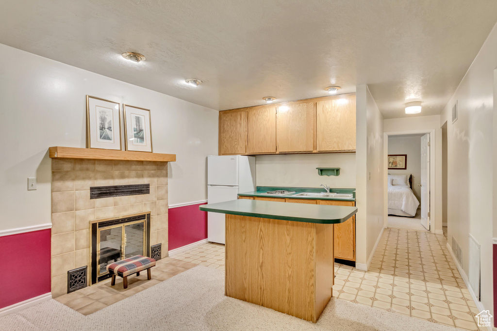 Kitchen with a kitchen island, a tile fireplace, and light carpet
