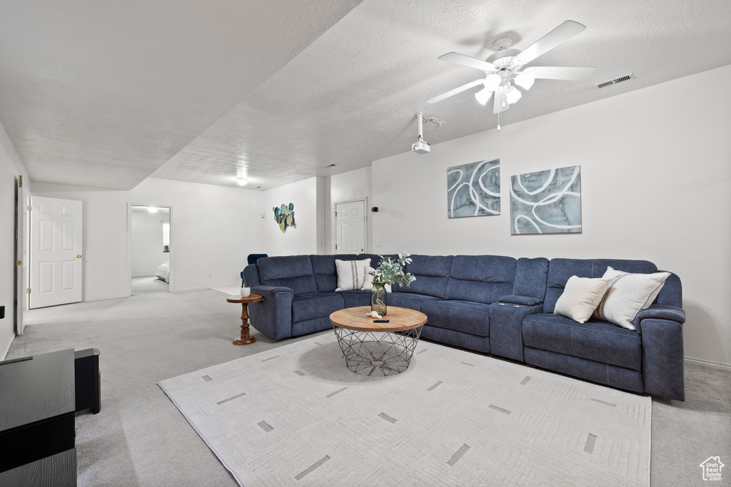 Living room with a textured ceiling, ceiling fan, and carpet floors