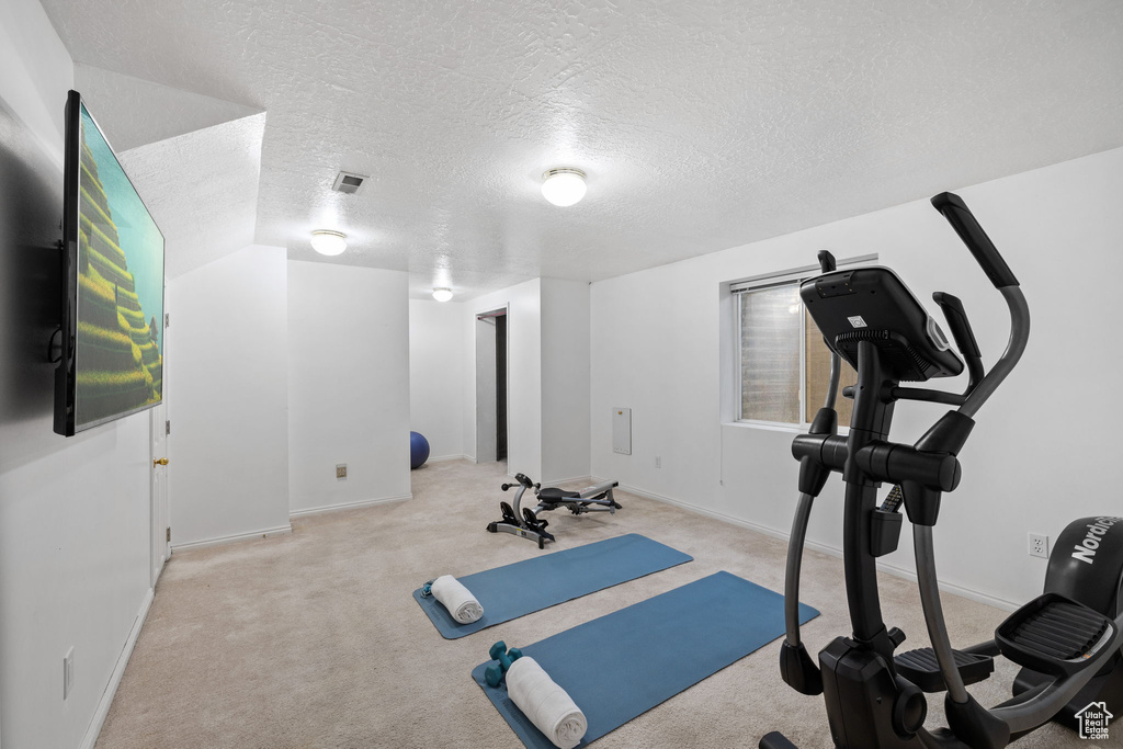 Workout area with light carpet, a textured ceiling, and lofted ceiling