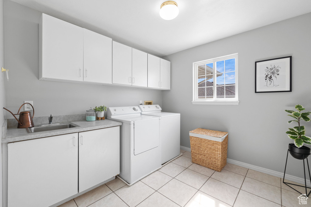 Laundry room featuring sink, light tile flooring, cabinets, and washer and clothes dryer