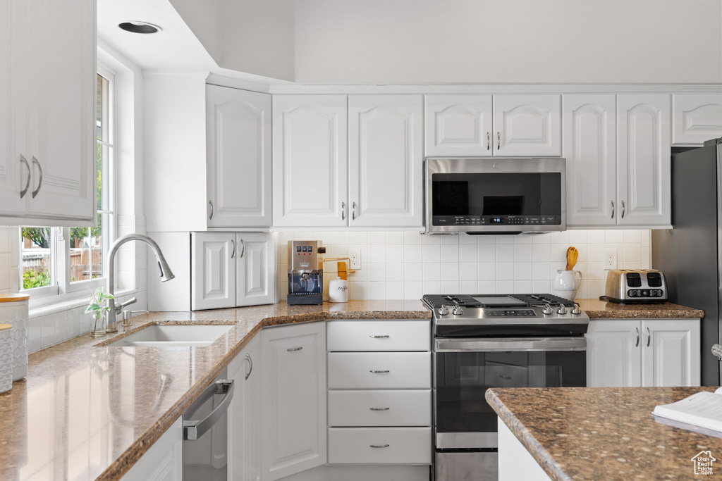 Kitchen featuring appliances with stainless steel finishes, stone countertops, tasteful backsplash, white cabinets, and sink