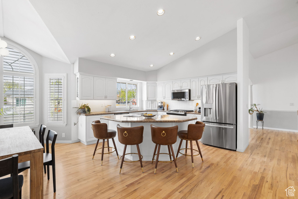 Kitchen featuring white cabinets, light hardwood / wood-style flooring, appliances with stainless steel finishes, a kitchen bar, and a kitchen island