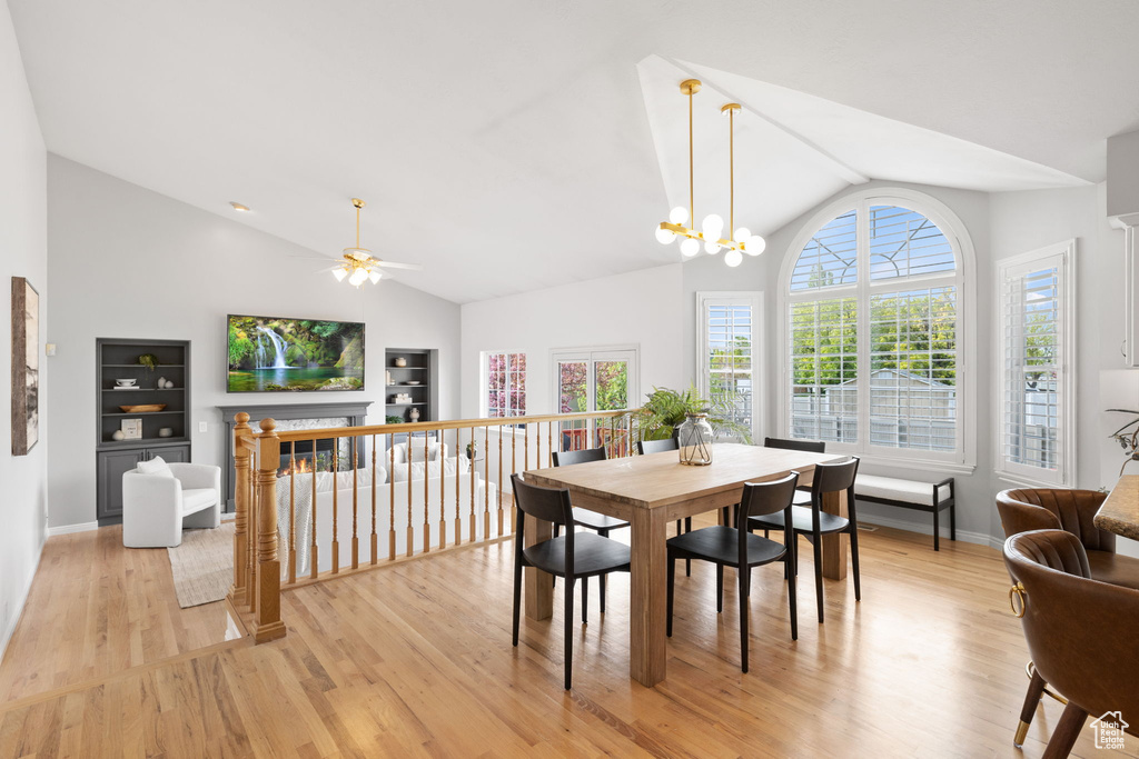 Dining area with ceiling fan with notable chandelier, high vaulted ceiling, light hardwood / wood-style floors, and built in features