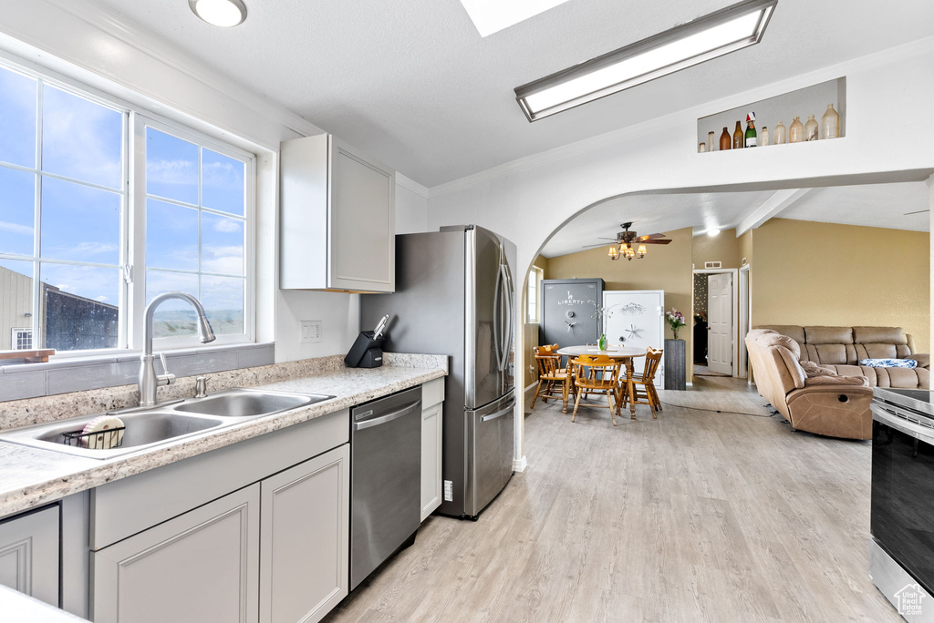 Kitchen featuring appliances with stainless steel finishes, light hardwood / wood-style flooring, ceiling fan, lofted ceiling with skylight, and sink
