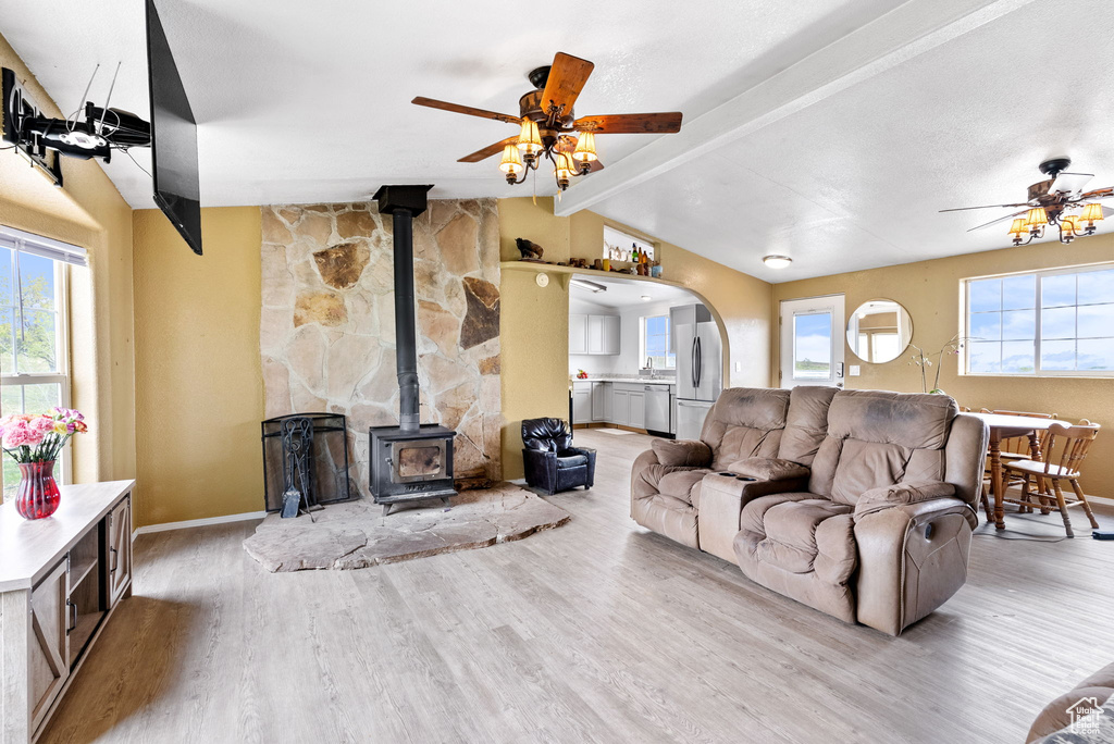 Living room featuring a wood stove, vaulted ceiling with beams, ceiling fan, and hardwood / wood-style floors