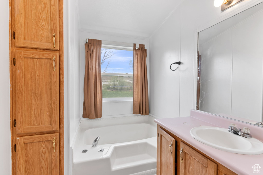 Bathroom featuring ornamental molding, vanity, and a bath to relax in
