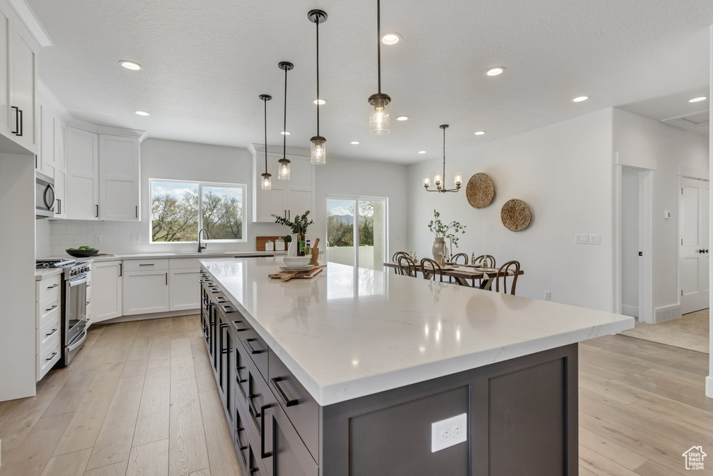 Kitchen with a center island, light wood-type flooring, white cabinetry, decorative light fixtures, and stainless steel appliances